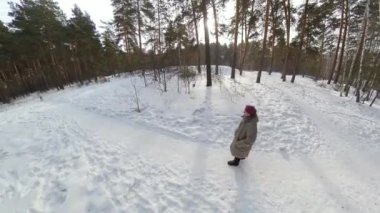 Kış ormanındaki büyükanne. Büyükannem bir çam parkında karla kaplı bir patika boyunca yürüyor. Kamera ondan uzaklaşıyor..