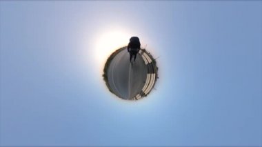 Bisiklet sürmek. Küçük gezegen. 360 derece kamera. Bisikletçi yol boyunca gezer. Güneş ufkun ötesinde batıyor. İyi akşamlar..