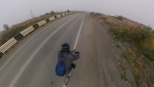 自転車利用 最上階だ サイクリストは霧の多い天気で高速道路に乗る カメラは彼を追いかけ 上から彼を撃つ — ストック動画