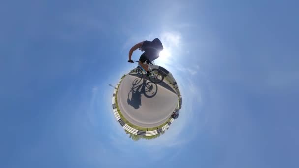 自転車利用 小さな惑星の眺め 360度カメラ 自転車は高速道路を速く走る 雲一つない空が小さな惑星を取り囲み — ストック動画