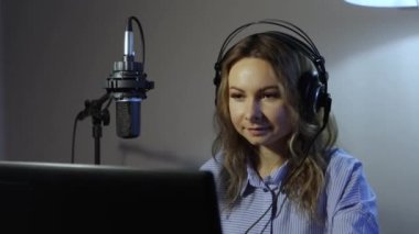 Evden canlı yayın. 2 Shot. Odasında güzel bir kız video blogu çekiyor. Kulaklık takar, mikrofonu kendisine doğru çeker ve seyirciyi selamlar. Yakın çekim ve orta çekim..