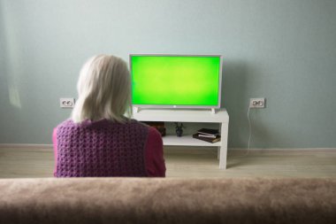 Büyükannem televizyon izliyor. Yeşil ekran. Gri saçlı bir büyükanne evdeki kanepede oturur. Önünde yeşil ekran bir televizyon var.. 