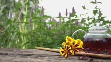 Doğada çay. Ağır çekim 2x. Çiçek açan nane arkaplanındaki amber çayıyla hayat devam ediyor. Bir adamın eli bir fincan çay alır. Kameranın yatay hareketi..