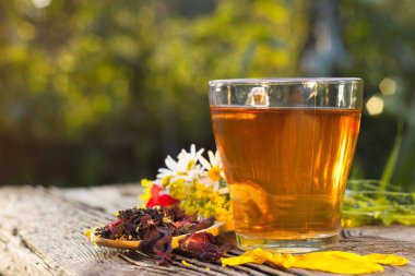 Doğada bitki çayı. Bulanık bir arka planda bitkisel çay (siyah çay, amber çayı, karanfil, kardomon, tarçın) ile yaşam devam ediyor. Hazırlanmış çay, kuru çay, gül yaprakları ve papatya çayı eski ahşap bir masada..