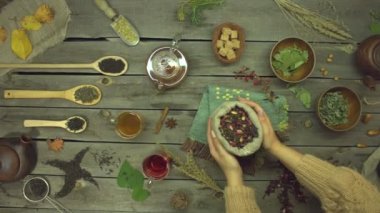 Eski ahşap bir masanın üzerindeki gül yapraklarından yapılan kırmızı çay. Düz yatıyordu. Farklı çay çeşitleriyle yaşam: siyah, yeşil, mat, amber çiçeği, meyve, bitkisel. Kadın eli masaya bir poşet amber çayı koydu. Yavaş çekim 2x.
