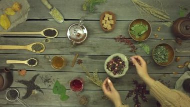 Eski ahşap bir masanın üzerindeki gül yapraklarından yapılan kırmızı çay. Düz yatıyordu. Farklı çay çeşitleriyle yaşam: siyah, yeşil, mat, amber çiçeği, meyve, bitkisel. Kadın eli, masadan bir poşet amber çayı alır. Yavaş çekim 2x.