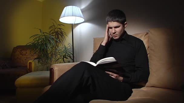 O tipo sentado no sofá à procura de algo no livro. . — Vídeo de Stock