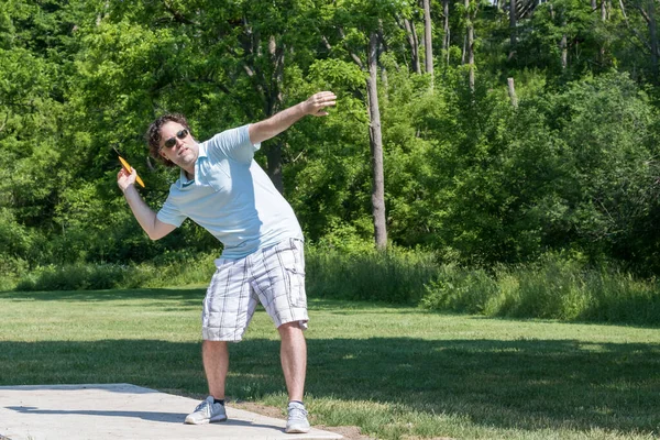 Middle aged Caucasian man in shorts, golf shirt, and sunglasses, preparing to throw a yellow disc in disc golf game. Lining up his shot.