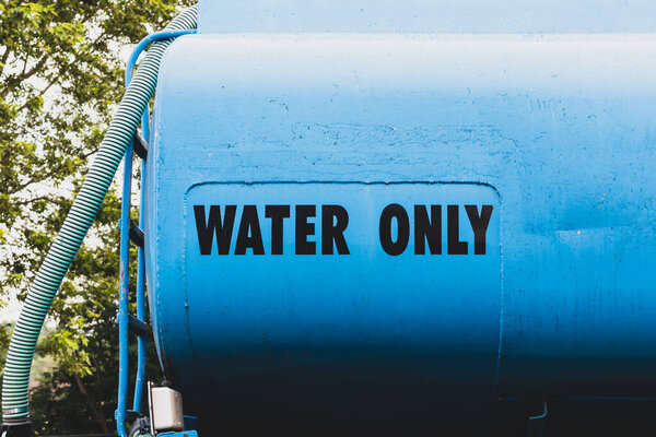 The words 'water only' written on the side of a blue water truck used for construction sites. Hose on side of truck.