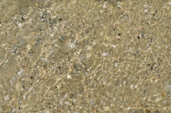 Ondas de água cristalina do mar cintilantes ao sol do meio-dia. Água ondulada com areia de fundo e conchas vistas debaixo d 'água — Fotografia de Stock