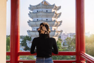 Arka planda yalnız genç bir kadının arka plan portresi. Doğanın arka planında sıcak bir ışıkla şehirde gün batımını seyrediyor. Hoş kız şehrin manzarasına ve balkondan kırsala bakıyor.