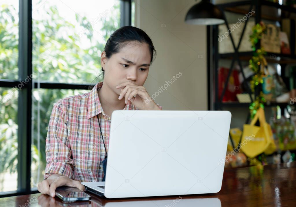 Young confused Asian woman working on laptop in cafe bar, thinking solving online problem solution. Thoughtful serious worried female focusing on computer screen and making decision. Lifestyle concept