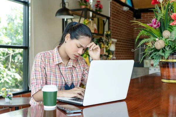 Young confused Asian woman working on laptop in cafe bar, thinking solving online problem solution. Thoughtful serious worried female focusing on computer screen and making decision. Lifestyle concept