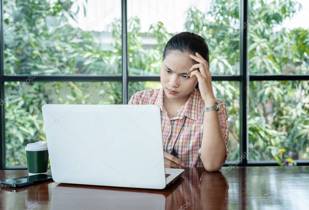 Young confused Asian woman working on laptop in cafe bar, thinking solving online problem solution. Thoughtful serious worried female focusing on computer screen and making decision. Lifestyle concept