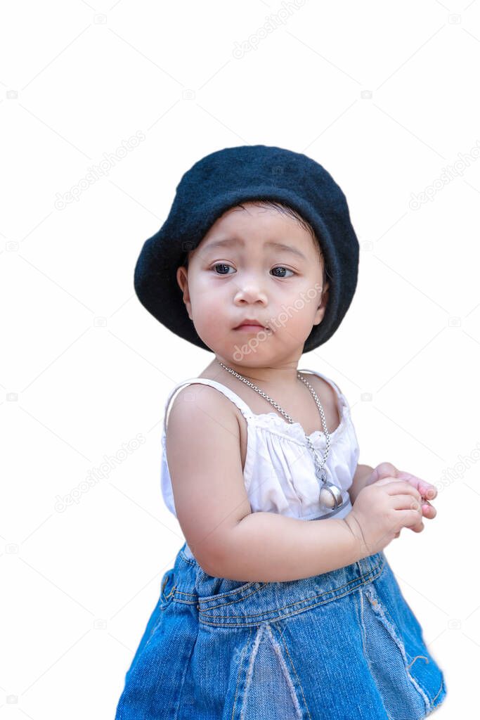 Adorable happy child girl standing and looking away to someone or something isolated on white background. Cute kid wears black hat, white dress and jean skirt looking to side and staring away thinking