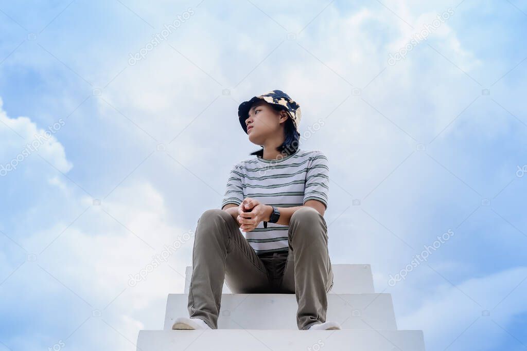 Thoughtful woman sitting alone at heaven white stairs for resting and finding inner peace with relaxation. Female looking away thinking about working moments with blue sky background. Freedom concept