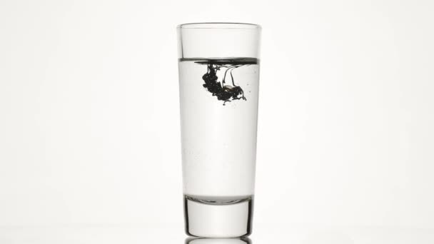 In un bicchiere d'acqua il colore liquido scuro scorre concettuale al rallentatore per bar — Video Stock