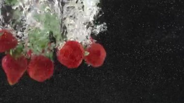 Çilek güzelliği siyah arka planda yavaş çekimde suya düşüyor.