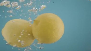 Sarı limon şeffaf suya düşüyor. Mavi arka plan. Taze meyve kabuğu.
