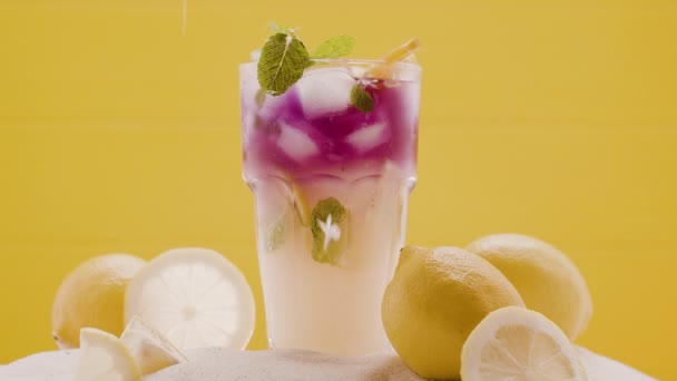 Cocktail en verre glacé limonade estivale rafraîchissante avec de nombreux pétales de fleurs de citrons — Video