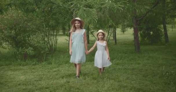 Irmãs bonitas caminham ao redor do parque sorrindo as crianças de mãos dadas — Vídeo de Stock