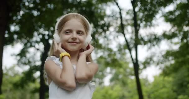 Niño pequeño escucha música en los auriculares modernos en el parque con relojes inteligentes — Vídeo de stock