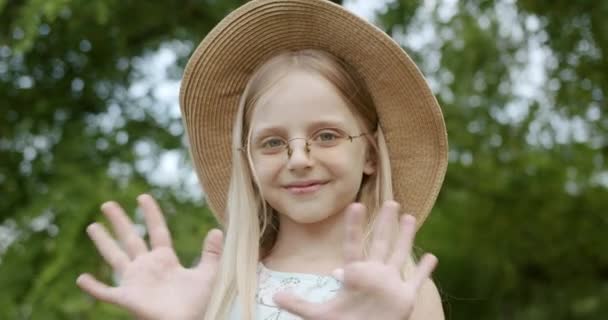Portret meisje Kijken naar camera zeggen hallo met blond haar en hoed en bril — Stockvideo