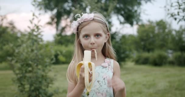 Retrato de una linda niña sin un diente sonriendo mientras come plátano — Vídeo de stock