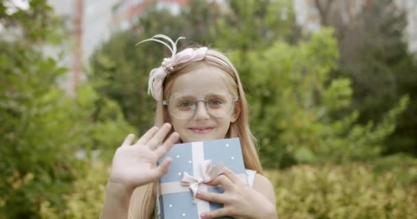 Ritratto ragazza guardando fotocamera dire ciao con una scatola regalo e occhiali — Video Stock