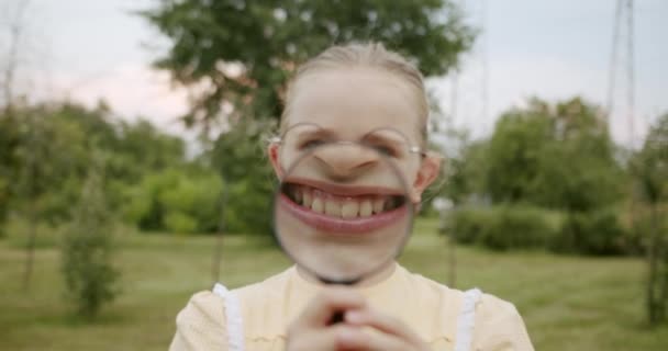 Loupe divertido niños sonríen con una lupa disfrutar de que hace grandes dientes — Vídeo de stock