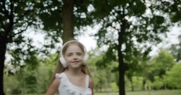 L'enfant heureux dansant en écoutant de la musique saute dans le parc oavec écouteurs — Video