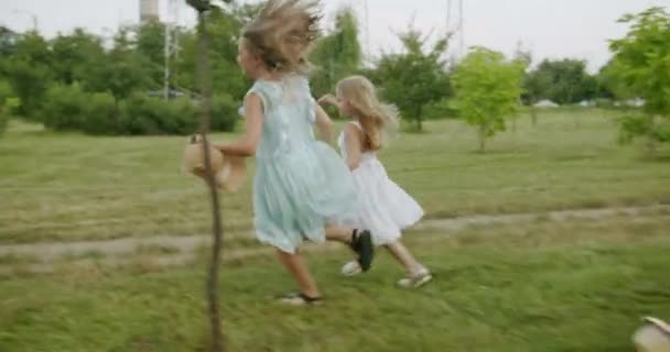 Glückliche Mädchen mit Hüten laufen durch den grünen Garten Kindertraum — Stockvideo