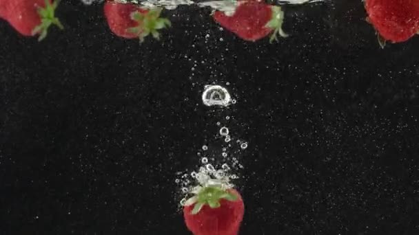 黒を背景にスローモーションで水の中に美しいイチゴ — ストック動画