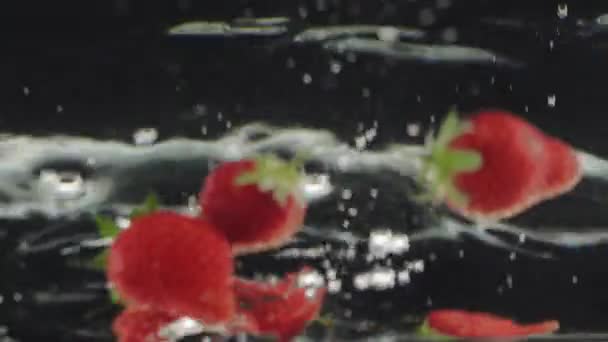 Verse aardbeien spetteren vallen in water op slow motion met reflecties — Stockvideo