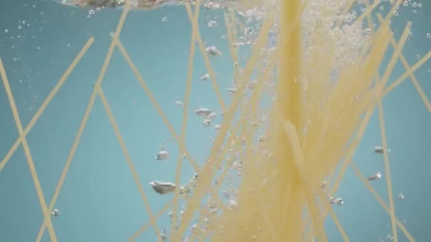 Спагетти бросают в воду на голубом фоне Паста падает в воду — стоковое видео