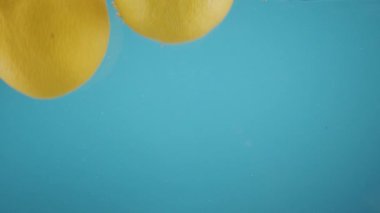 Sarı limon şeffaf suya düşüyor. Mavi arka plan. Taze meyve kabuğu.