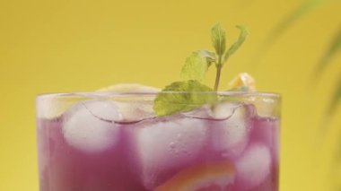 Limonata menekşe kokteyli, ferahlatıcı yaz, sarı arka planda buz naneli.