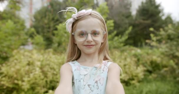 Маленька дівчинка посміхається в окулярах дарує подарункову коробку і посміхається парковій природі — стокове відео
