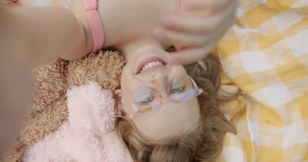 La chica con gafas de color rosa se hace sonreír a la naturaleza en una manta amarilla — Vídeo de stock