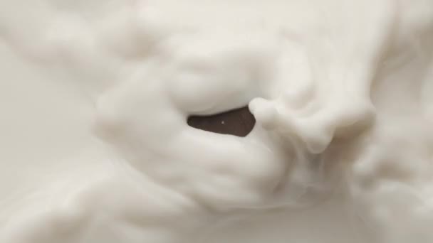 Chocolate quadrado caindo em uma tigela de leite e fazendo coroa e ondulações circulares — Vídeo de Stock