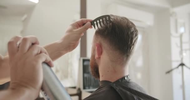 Maschio attraente sta ottenendo un taglio di capelli moderno in negozio di barbiere, fissaggio dei capelli a spruzzo — Video Stock