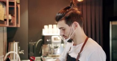Barista iş yerinde, bir fincan koyu kahve yapıyor ve terminalde ödeme yapıyor.