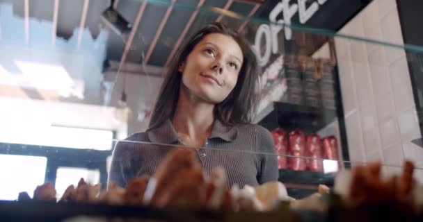 Ein schönes Mädchen sucht und wählt Croissants und Kaffee im Café kaufen — Stockvideo