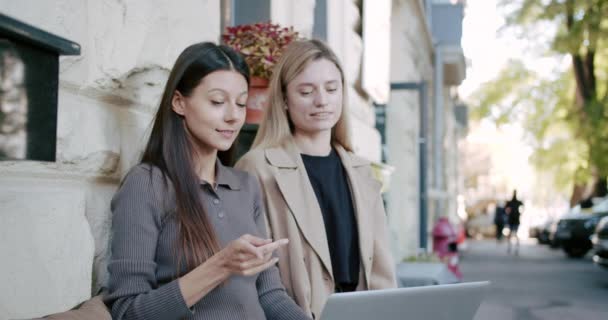 两个漂亮的女孩正在一个项目上工作，在外面的一家咖啡店附近聊天，一起锻炼 — 图库视频影像