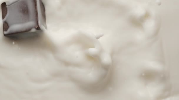 Квадратний шоколад падає в розтоплений йогурт і робить коронку і кругові брижі — стокове відео