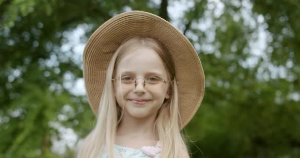 Schattig klein meisje model met bril en hoed, glimlachen en kijkt in camera in park — Stockvideo