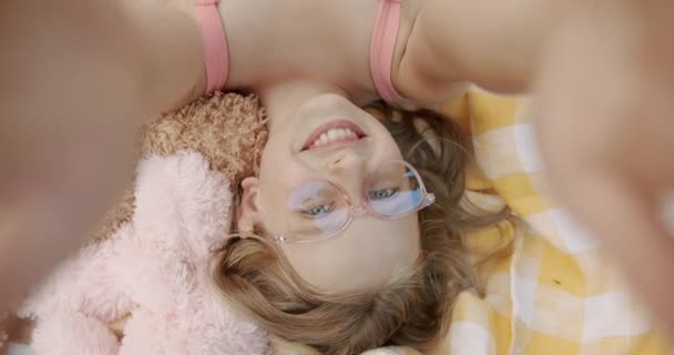 Fata cu ochelari roz se face zâmbind la mare pe o pătură galbenă — Videoclip de stoc