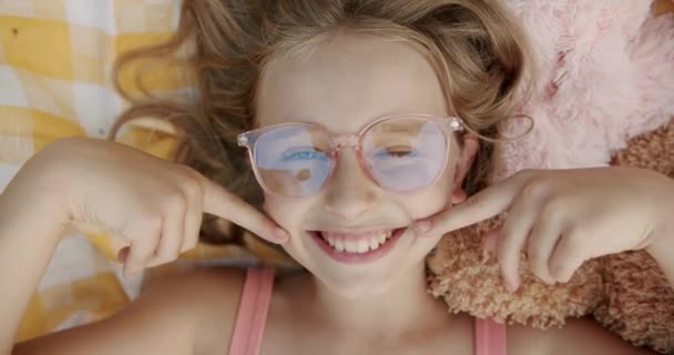 Schattig meisje met bril maakt een mooie glimlach met de handen op een gele deken — Stockvideo