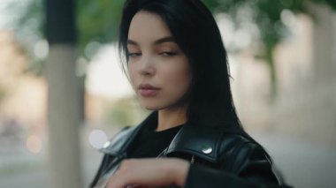 Deri ceketli, açık havada poz veren kendinden emin genç bir kadının portresi. Yumuşak odak arkaplanı görüntüye sanatsal bir dokunuş ekler, bu da bağımsızlığı ve modern tarzı gösterir..