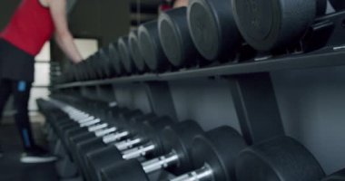 Modern Spor Salonu 'nda Dambılları Seçmeye Odaklanmış Atletizm. Spor salonunun yakın plan görüntüsü, bir atletin dambılı kaldırışı, daha fazla ekipmanı gösteren odaklanmamış arka plan..